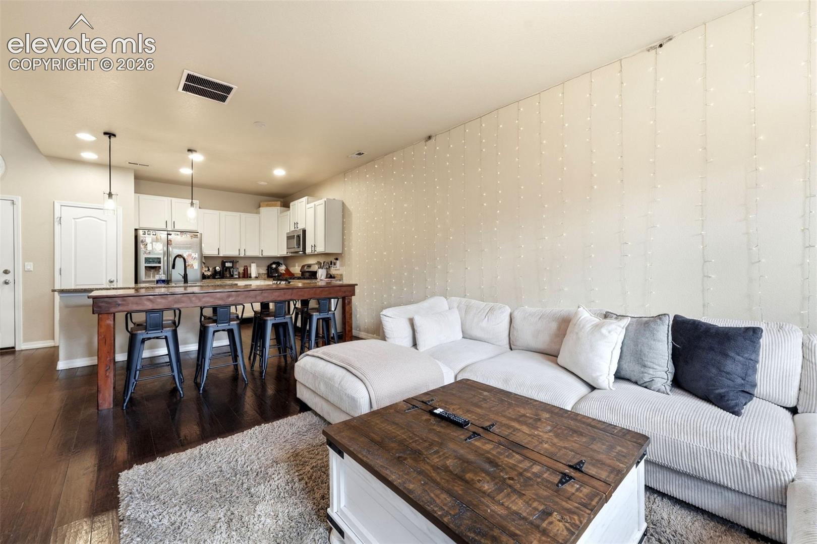 Open-concept living space featuring wood-finish flooring, recessed lighting, white cabinetry, and stainless steel appliances