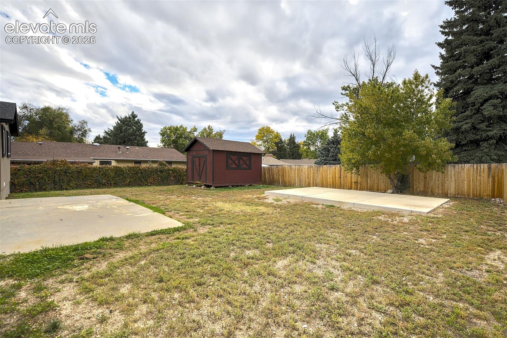 Expansive backyard featuring two concrete pads, a detached wood-frame storage shed, and a perimeter privacy fence