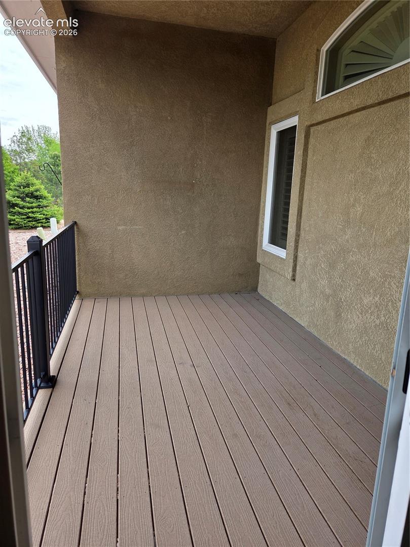 Outdoor patio featuring composite decking, stucco exterior, and a black wrought iron railing