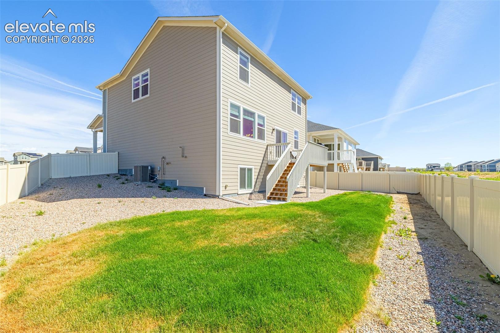 Two-story exterior with siding, a wooden deck with stairs, a green lawn, and a light-colored privacy fence