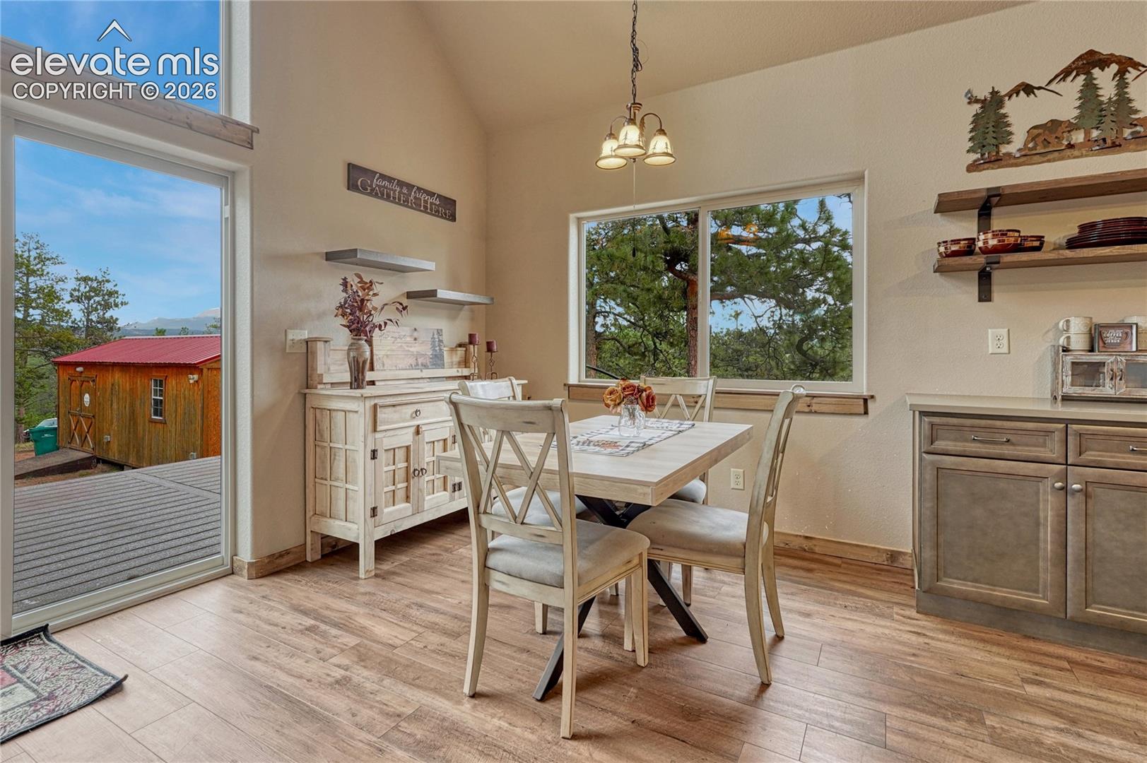 Vaulted ceilings featuring expansive windows, wood-finish flooring, built-in lower cabinetry, and fixed wooden shelving