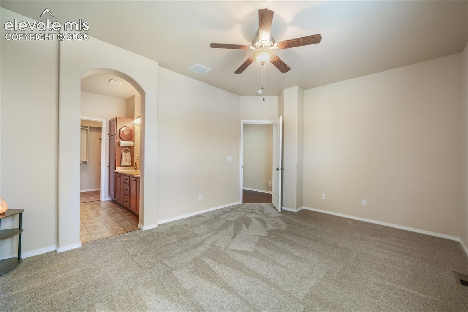 Carpeted flooring, arched doorway, ceiling fan with integrated lighting, wood vanity with integrated sink, tile flooring