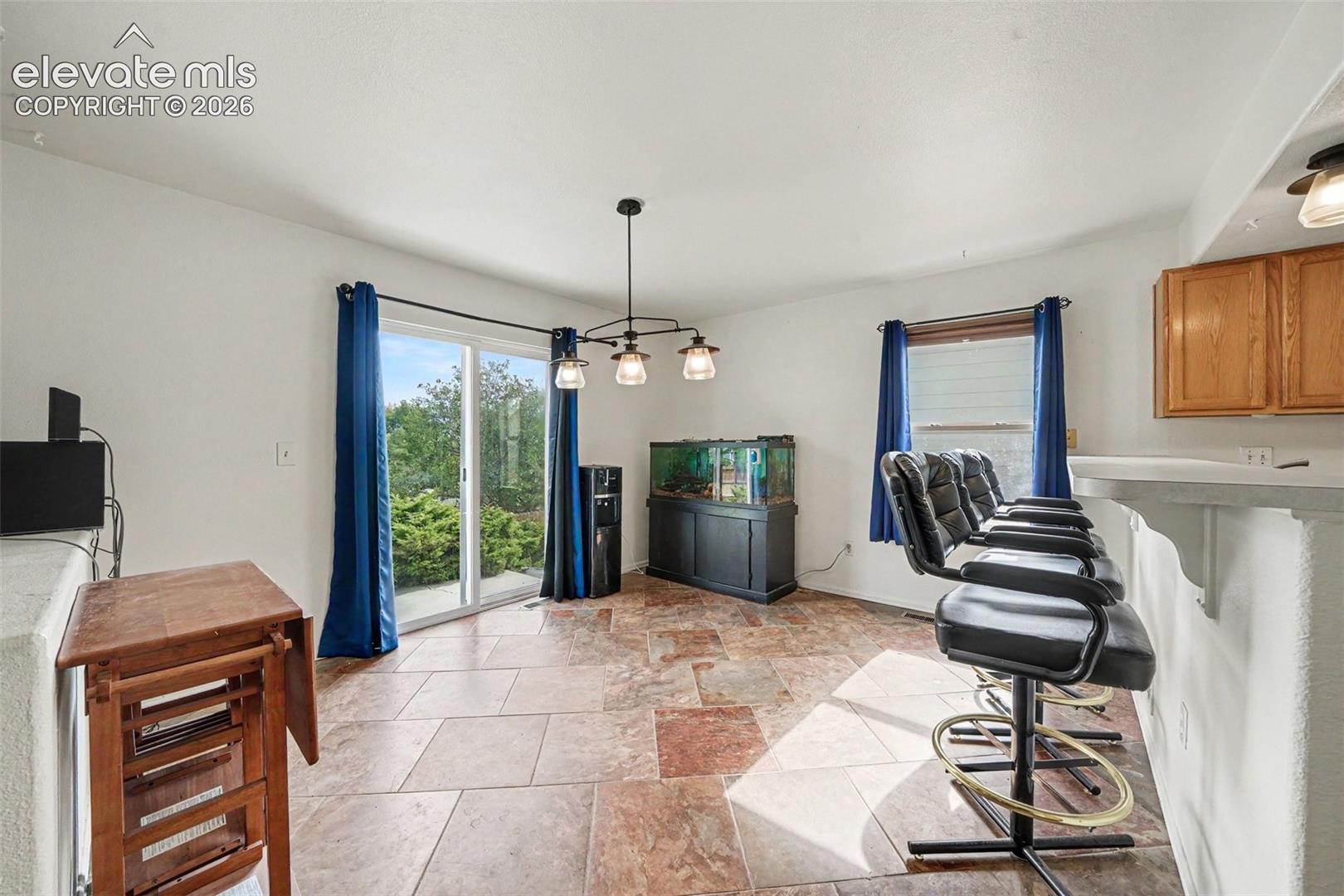 Stone-tile flooring, metal multi-light chandelier, and sliding glass patio door