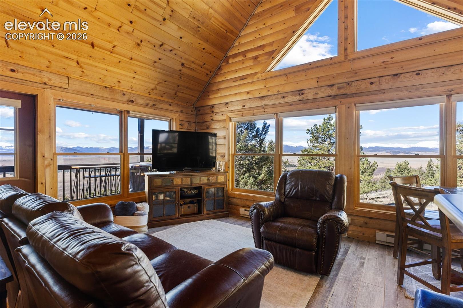 Vaulted ceilings with exposed timber walls, expansive floor-to-ceiling windows, and wood-finish flooring
