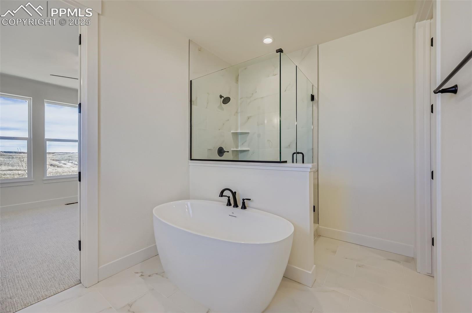 Bathroom featuring a marble finish shower, a freestanding bath, light marble finish flooring, and recessed lighting