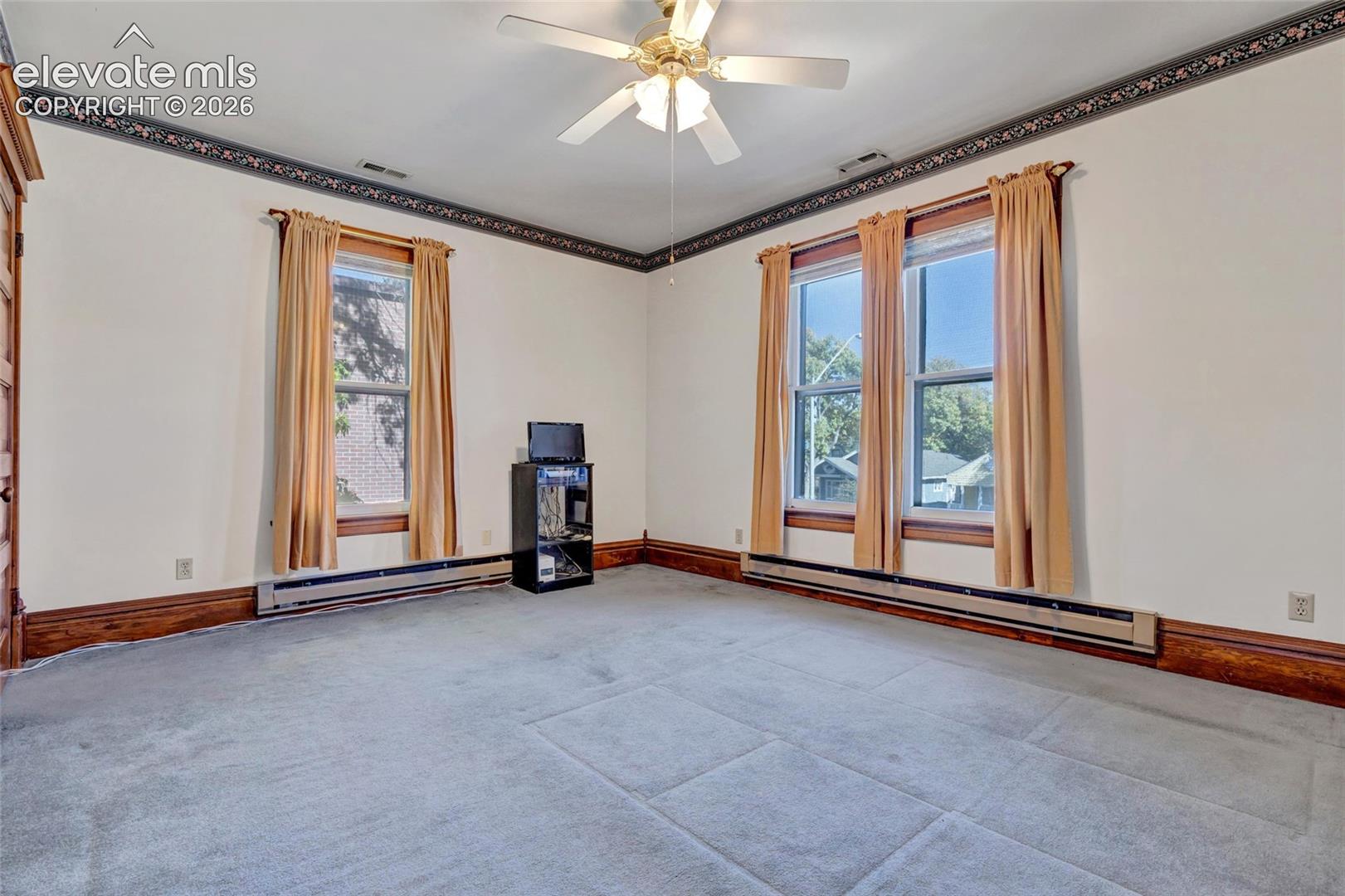 Room interior featuring large windows, intricate crown molding, dark wood trim, and a centered ceiling fan