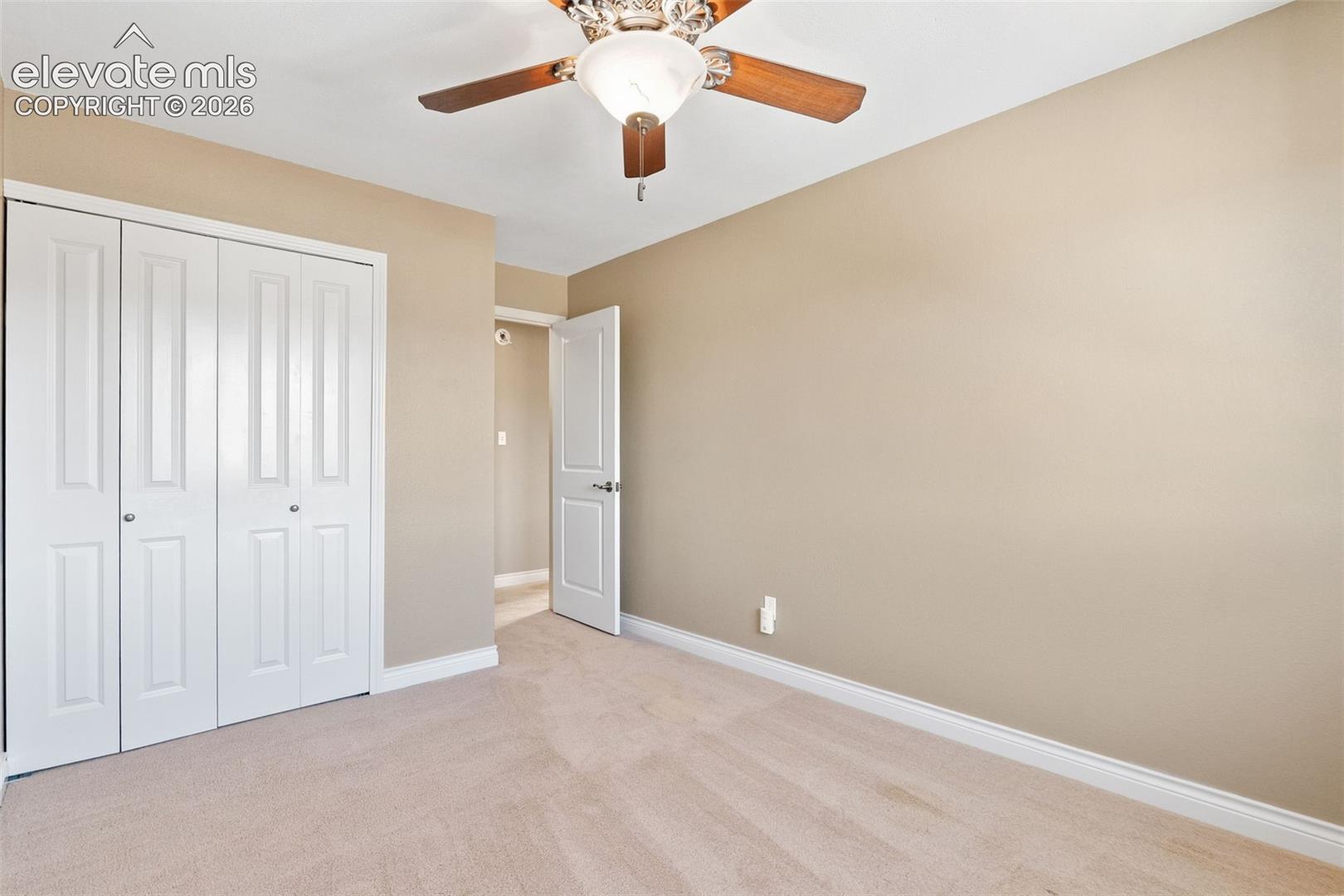 Neutral-toned interior featuring wall-to-wall carpeting, bi-fold closet doors, a multi-panel interior door, and a ceiling-mounted light fixture with a fan