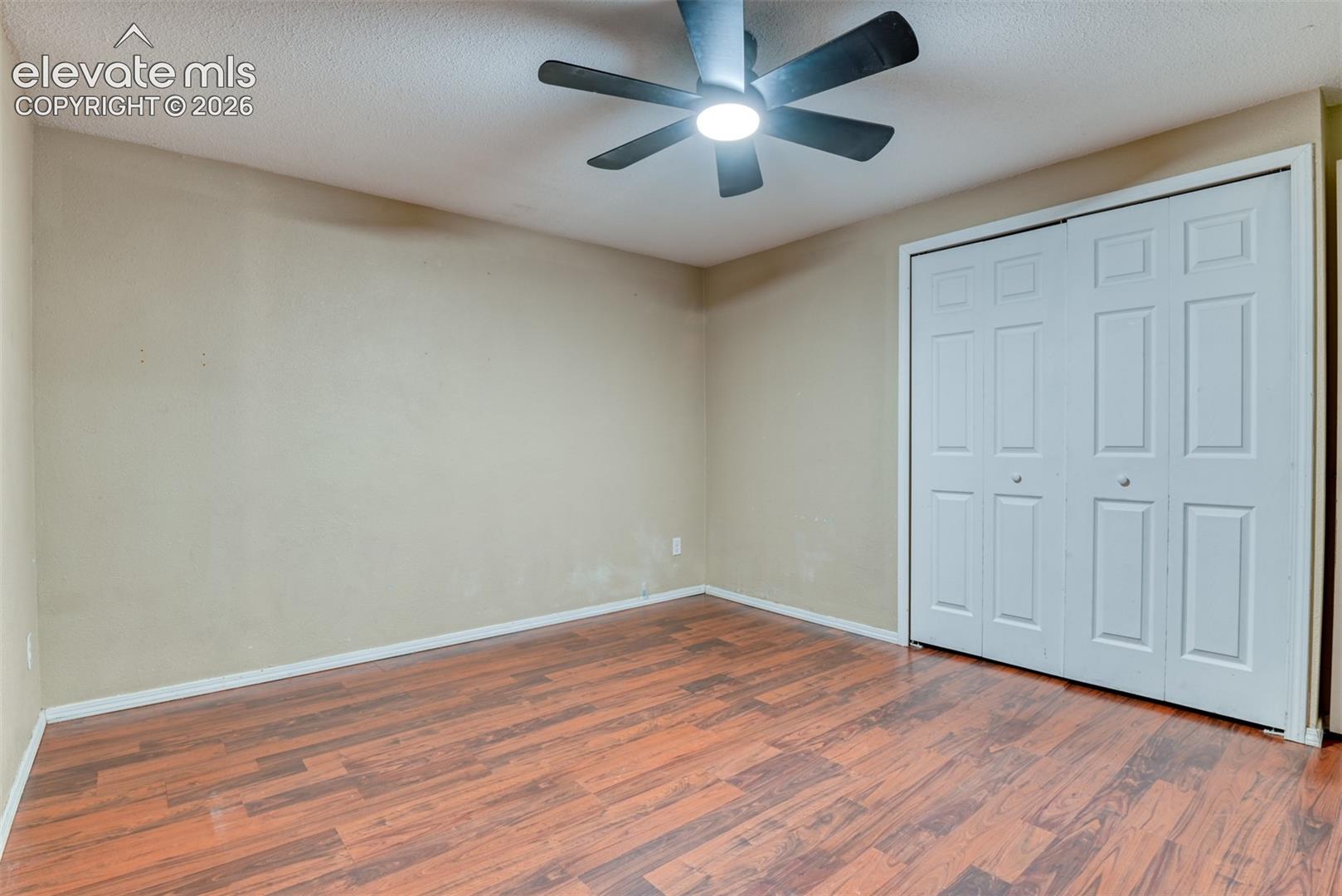 Room featuring wood-finish flooring, a ceiling fan with integrated lighting, and bi-fold closet doors