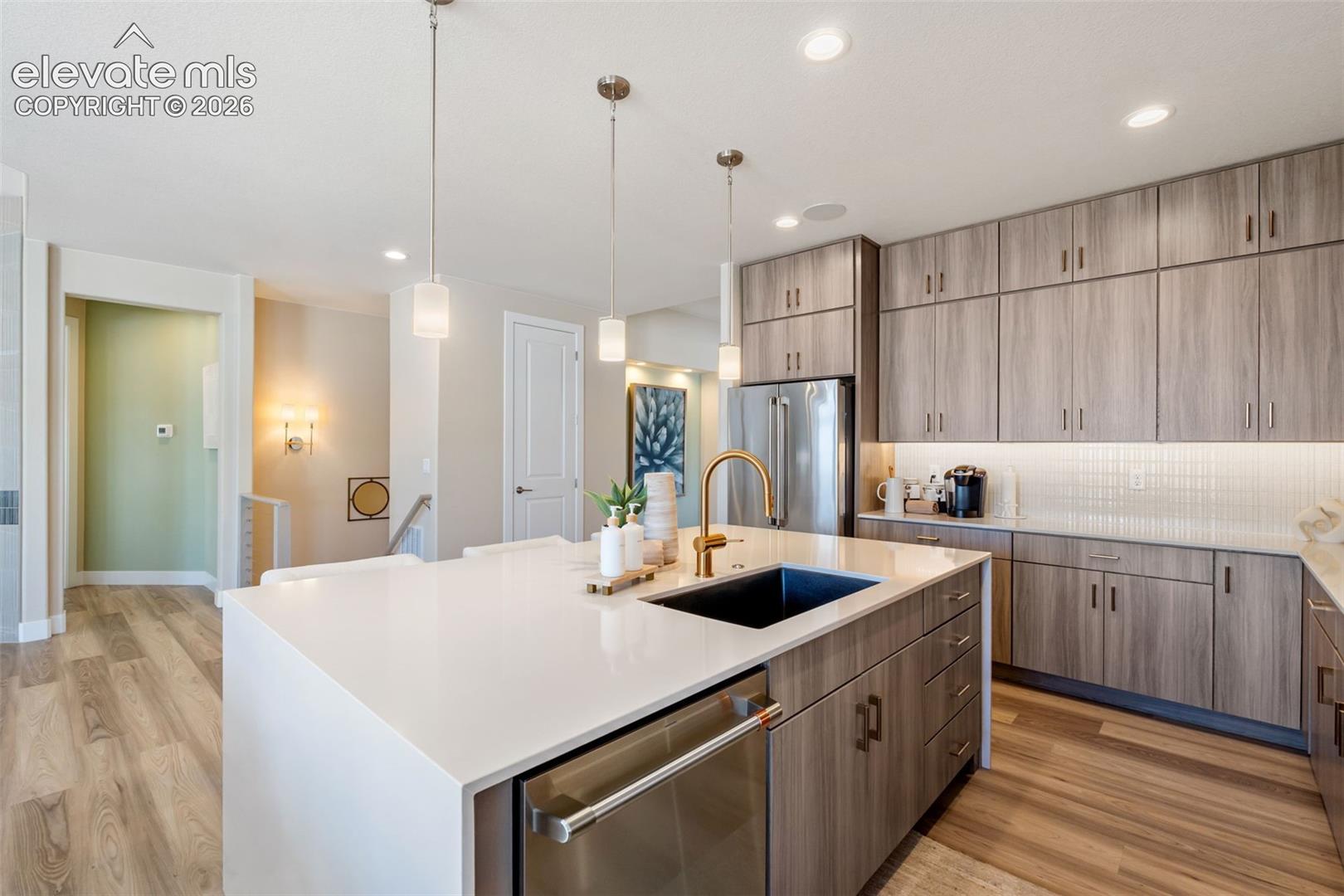 Kitchen featuring flat-panel wood-finish cabinetry, quartz countertops, an undermount sink with a brass-finish faucet, recessed lighting, and wood-finish flooring