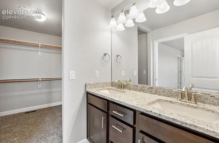 Double vanity featuring stone countertops, integrated porcelain sinks, dark cabinetry with satin nickel hardware, and an oversized vanity mirror with multi-light fixture