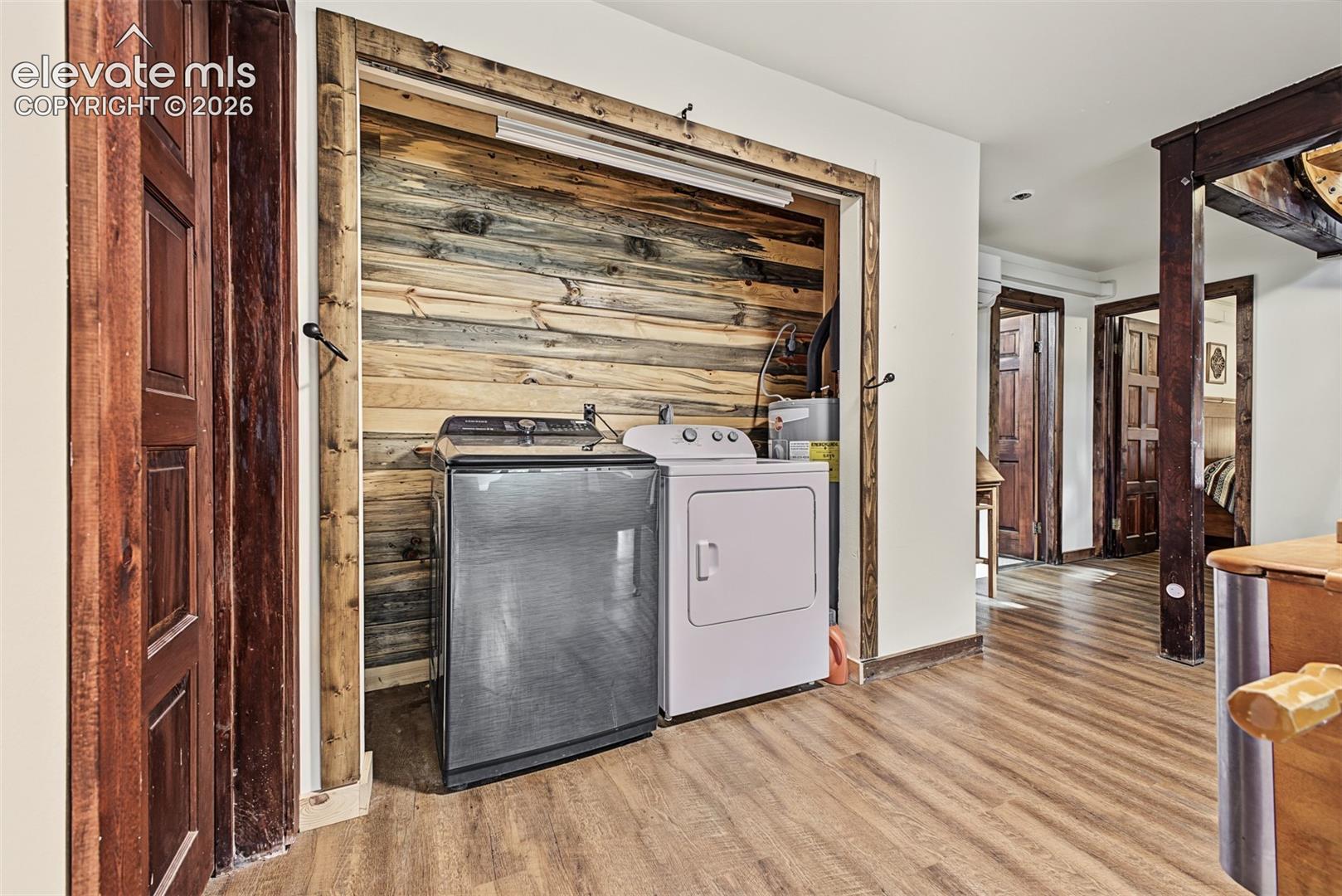 Laundry closet with wood plank backing, wood-finish flooring, and solid wood doors