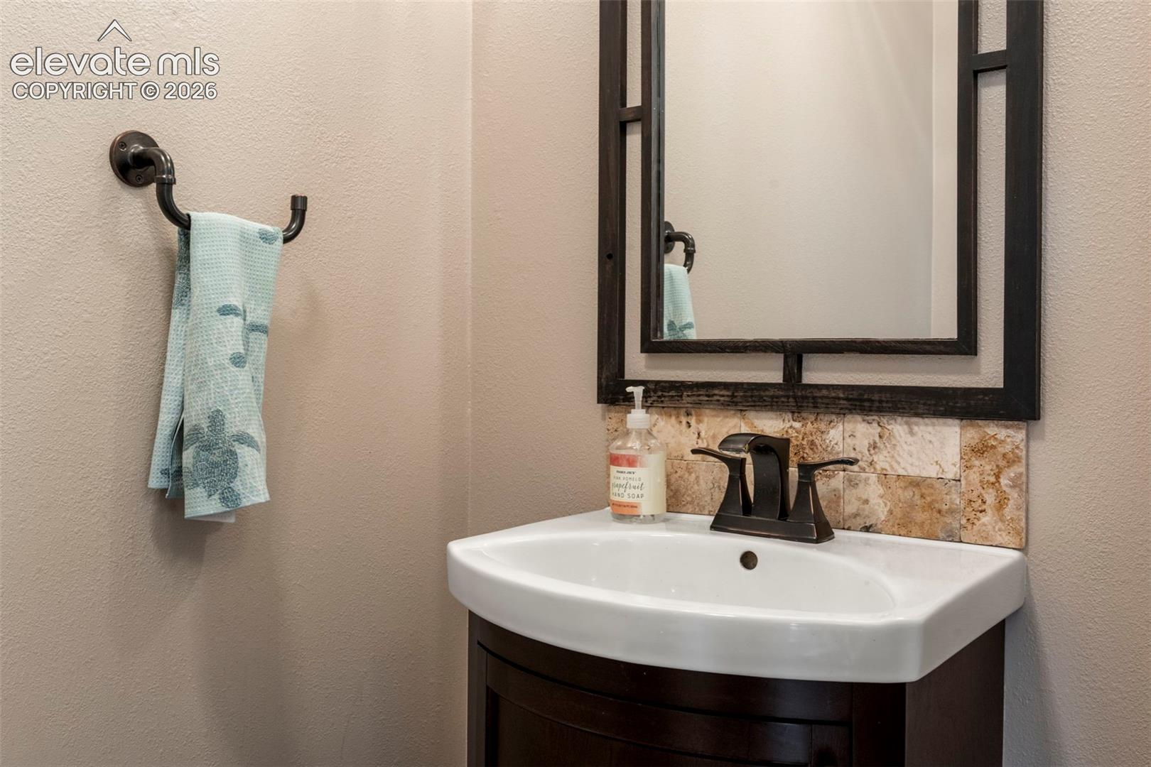 Half bathroom with vanity, a textured wall, and decorative backsplash