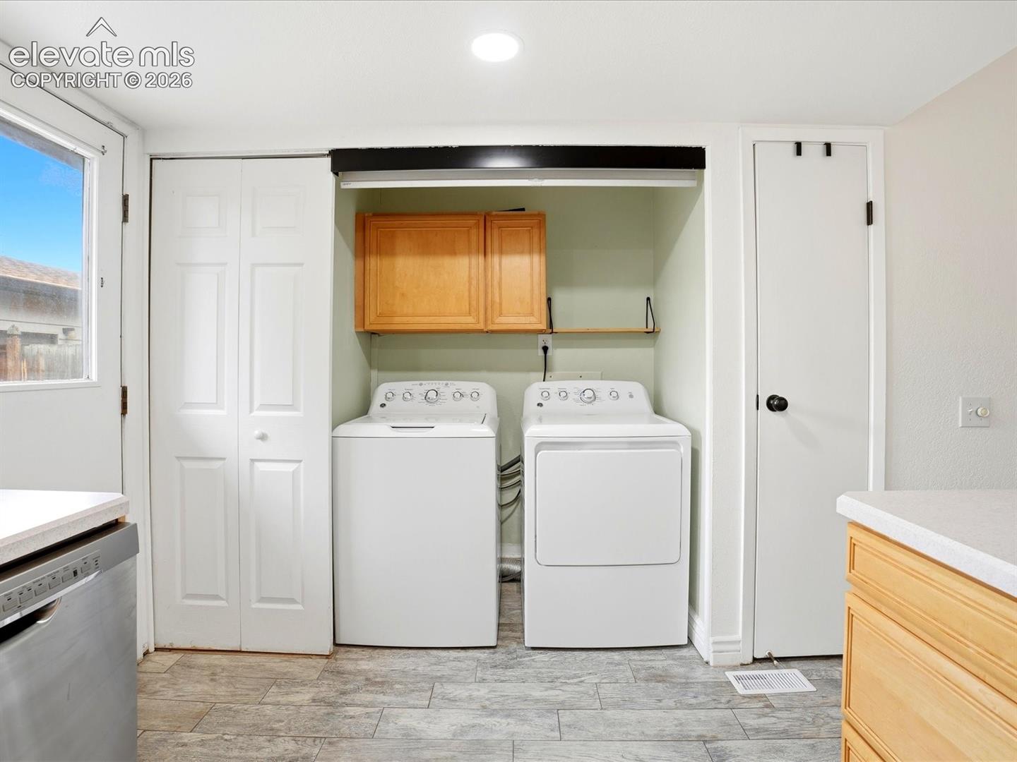 Laundry area featuring stone-finish tile flooring, wood-finish wall-mounted cabinetry, recessed lighting, and white bi-fold closet doors