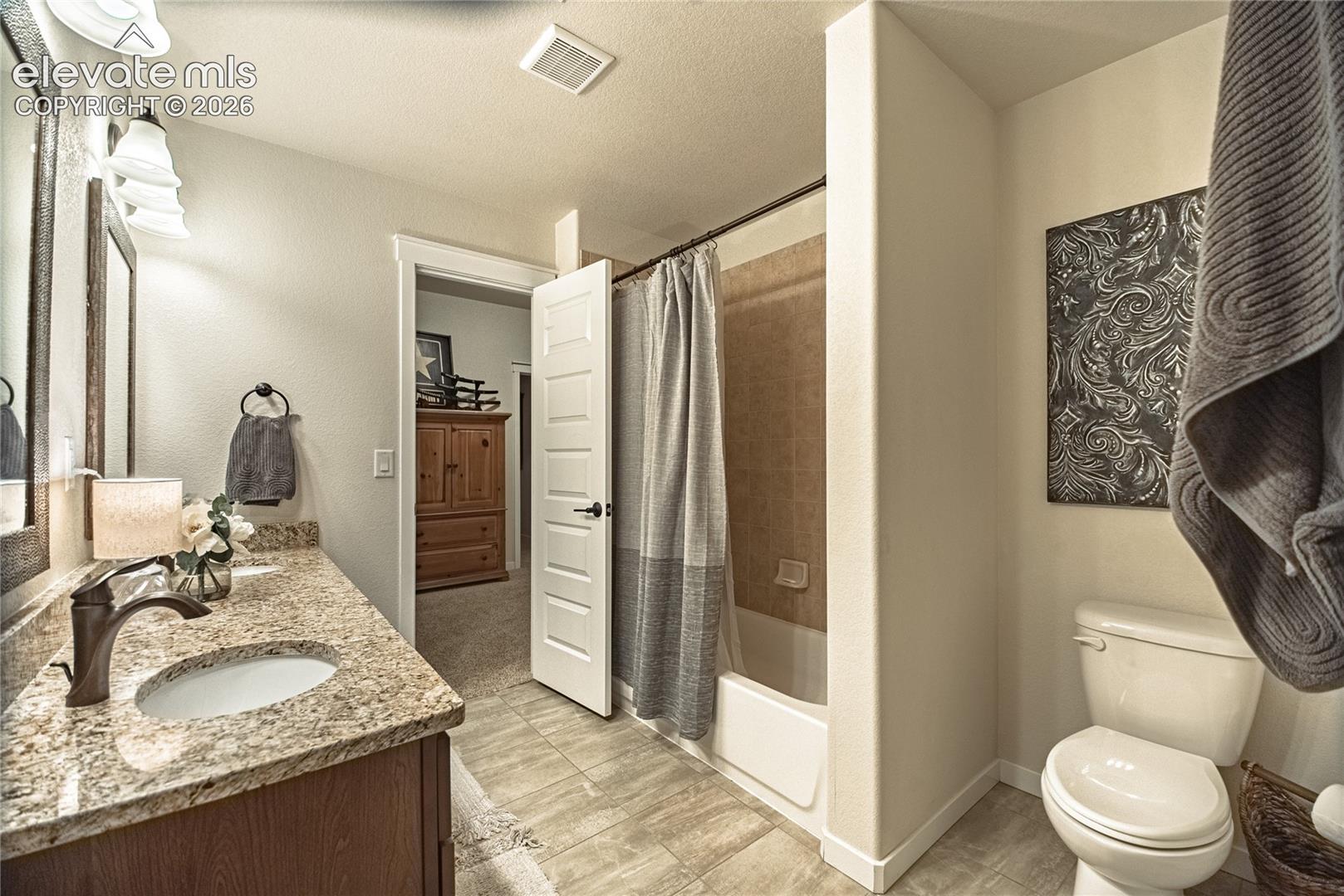 Bathroom featuring a stone-composite countertop, dark wood-finish vanity cabinetry, oil-rubbed bronze faucet, ceramic tile flooring, and a tub-shower combination with full-height wall surround