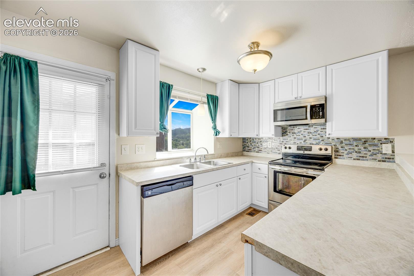 White cabinetry, stainless steel appliances, patterned tile backsplash, wood-finish flooring, and light-toned countertops