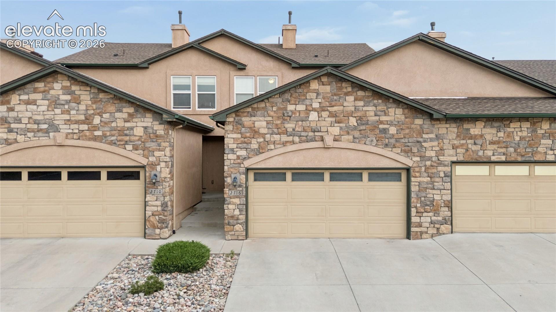 Stacked stone and stucco exterior featuring multiple garage bays with arched details and integrated windows