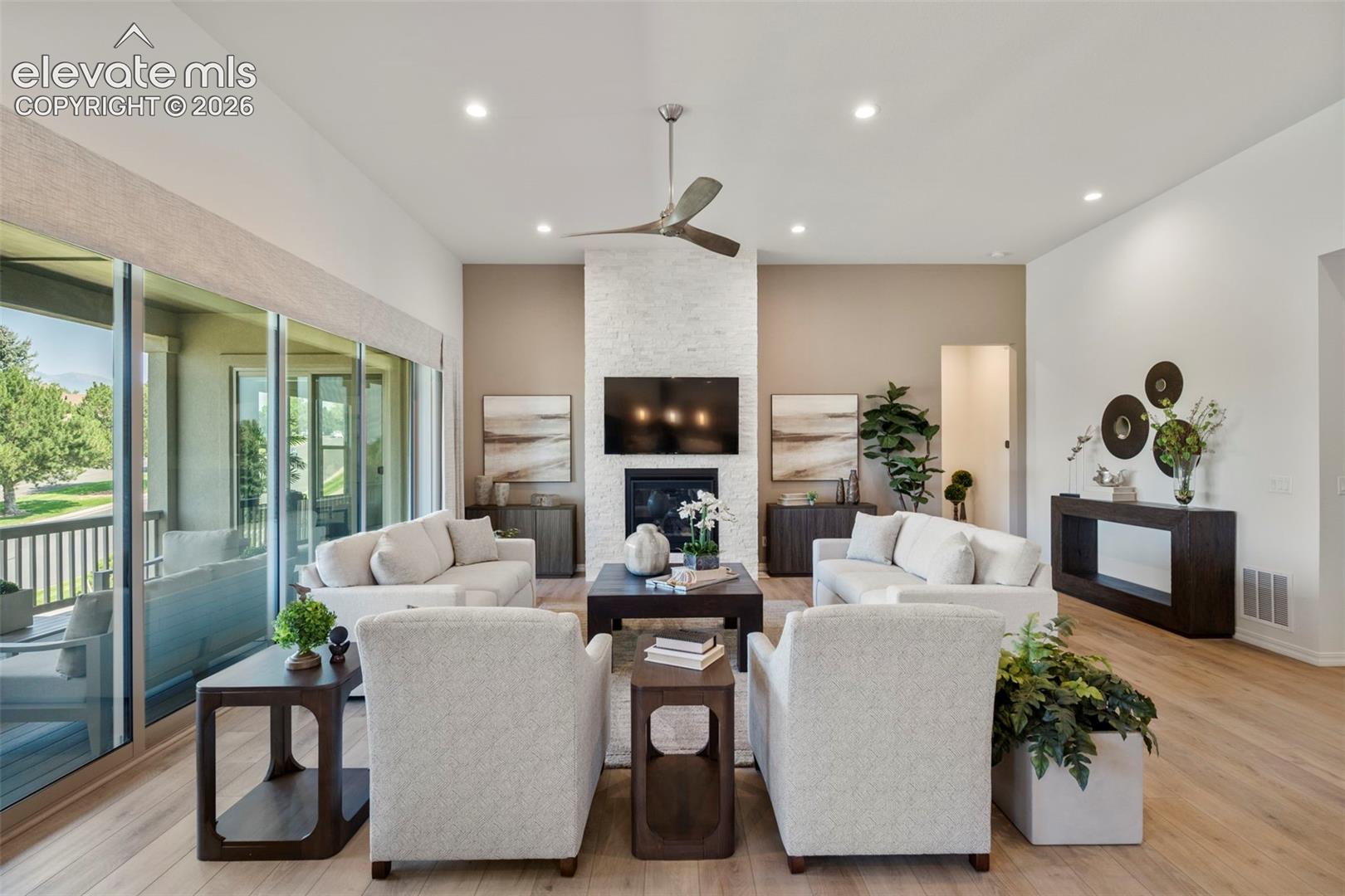 Spacious living area featuring beautiful flooring, a contemporary fireplace with a stacked stone surround, walk-out to covered deck bringing the outside in.