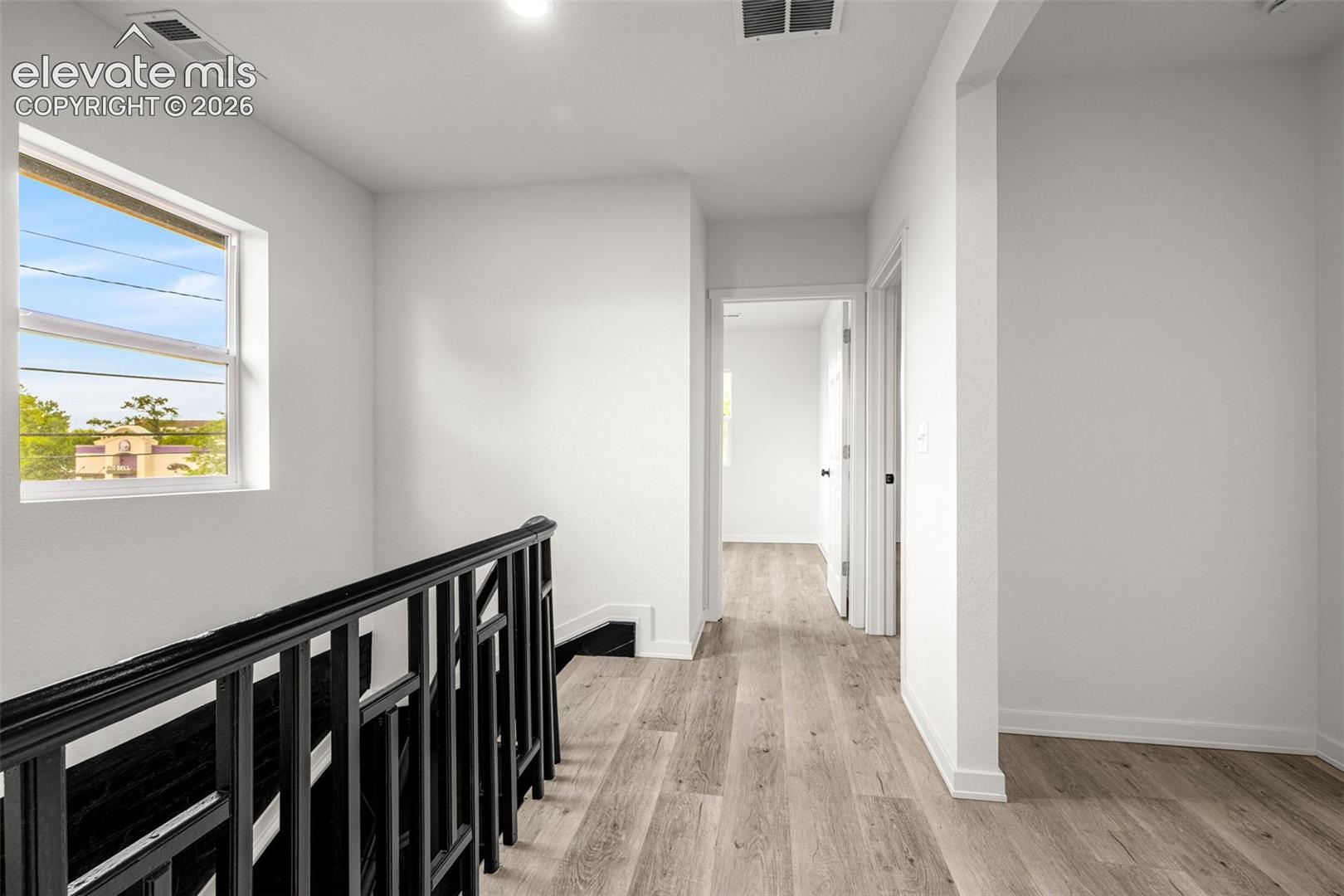 Upper-level hallway with wood-finish flooring, white walls, and recessed lighting