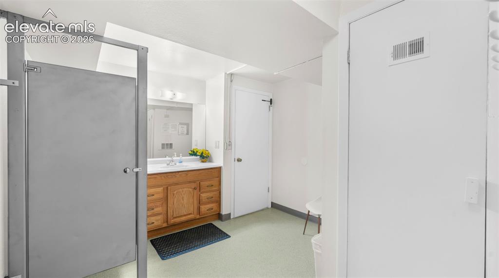 Bathroom featuring a wood vanity with a white countertop and rectangular sink, a mirrored wall, and overhead vanity lighting