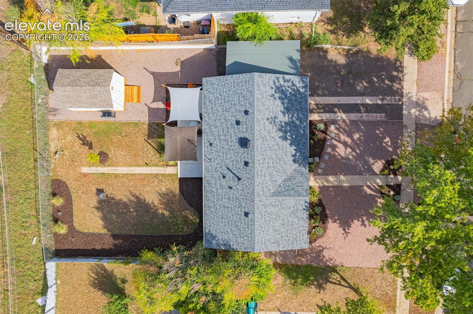 Gable roofline, detached shed, shade sails, gravel hardscaping, and landscaped beds