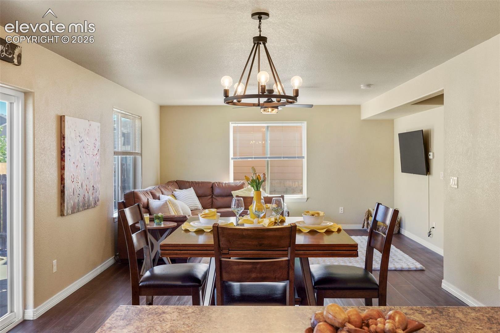 Open-concept living area featuring wood-finish flooring, a dining space with a chandelier, and a living area with multiple windows