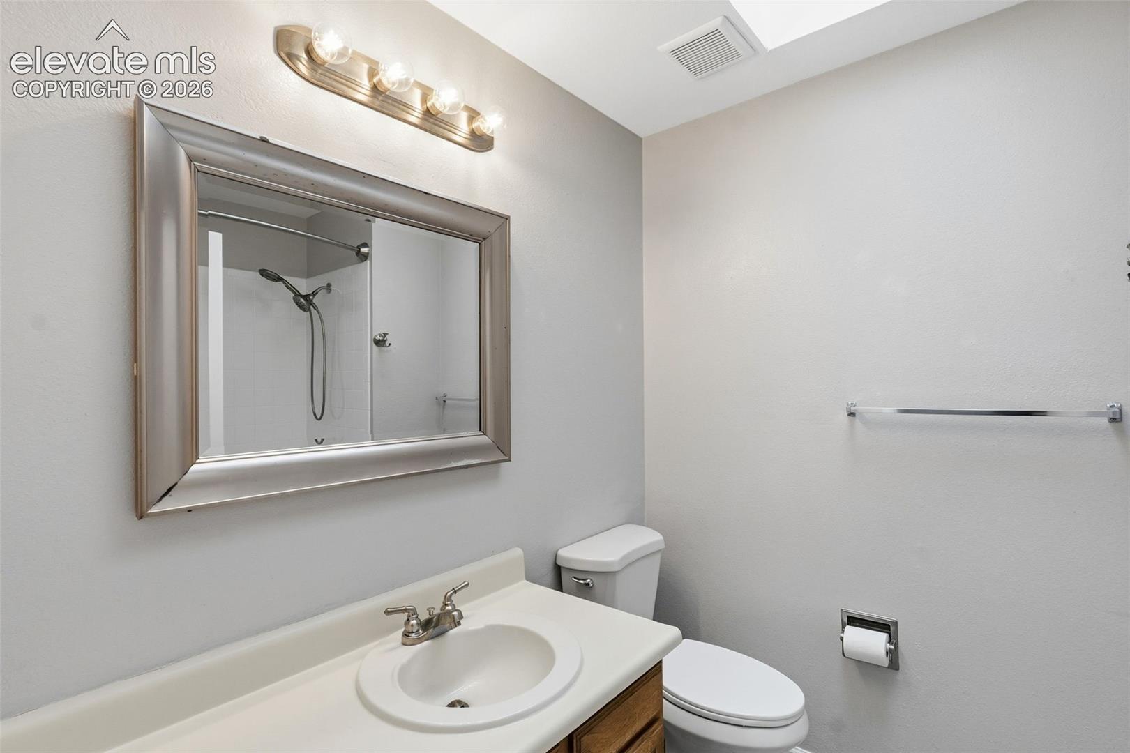 Vanity with integrated sink and chrome faucet, framed mirror with vanity lighting, and toilet