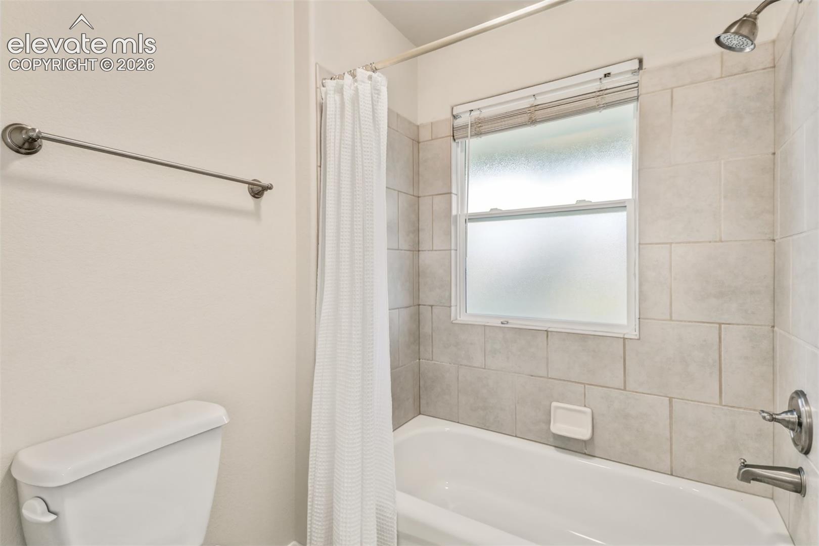 Bathroom featuring large-format ceramic wall tiling, a built-in bathtub with a wall-mounted showerhead, and a privacy-glass window
