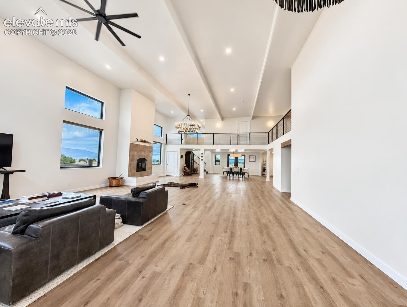 Expansive great room featuring high ceilings, wood-finish flooring, a tiled fireplace, recessed lighting, and a metal-railed mezzanine