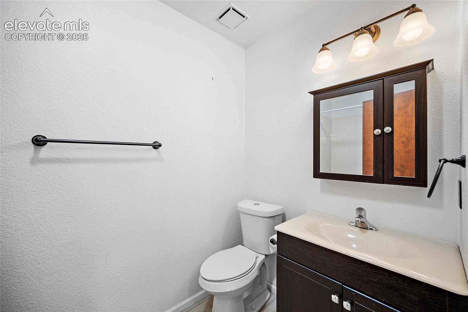 Bathroom featuring a dark wood-finish vanity with an integrated sink, coordinating dark wood-finish medicine cabinet with mirror, and a three-light vanity fixture with frosted glass shades