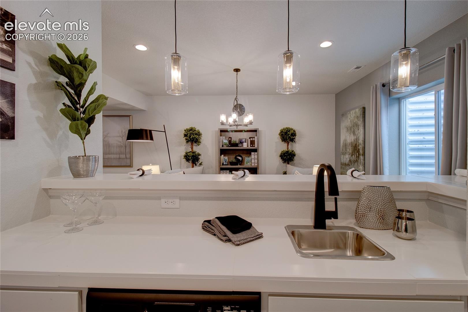Countertop with a matte black high-arc faucet, undermount stainless steel sink, recessed lighting, and clear glass pendant fixtures