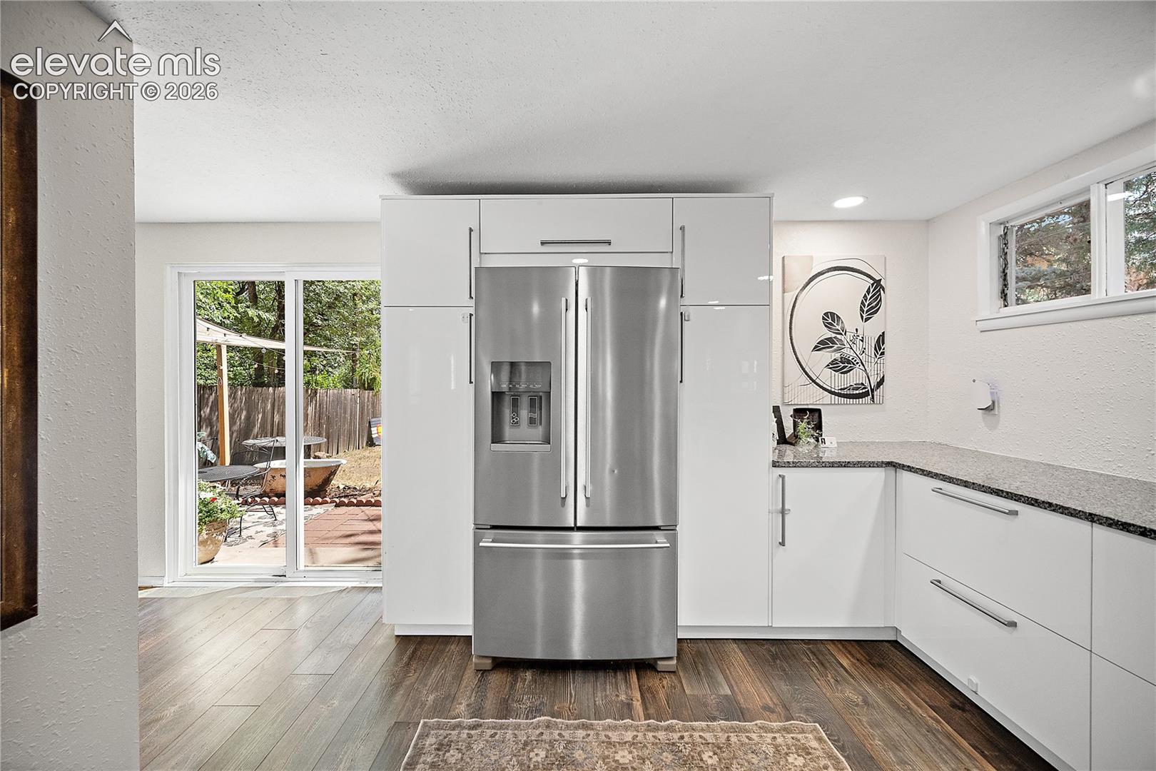 Contemporary kitchen featuring a stainless steel French-door refrigerator, sleek white cabinetry, and a dark speckled countertop