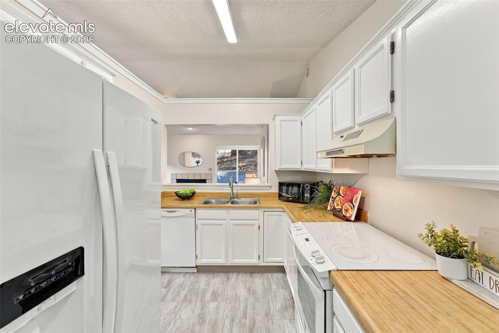 Kitchen featuring white cabinetry, wood-finish countertops, dual-basin stainless steel sink, and wood-finish flooring
