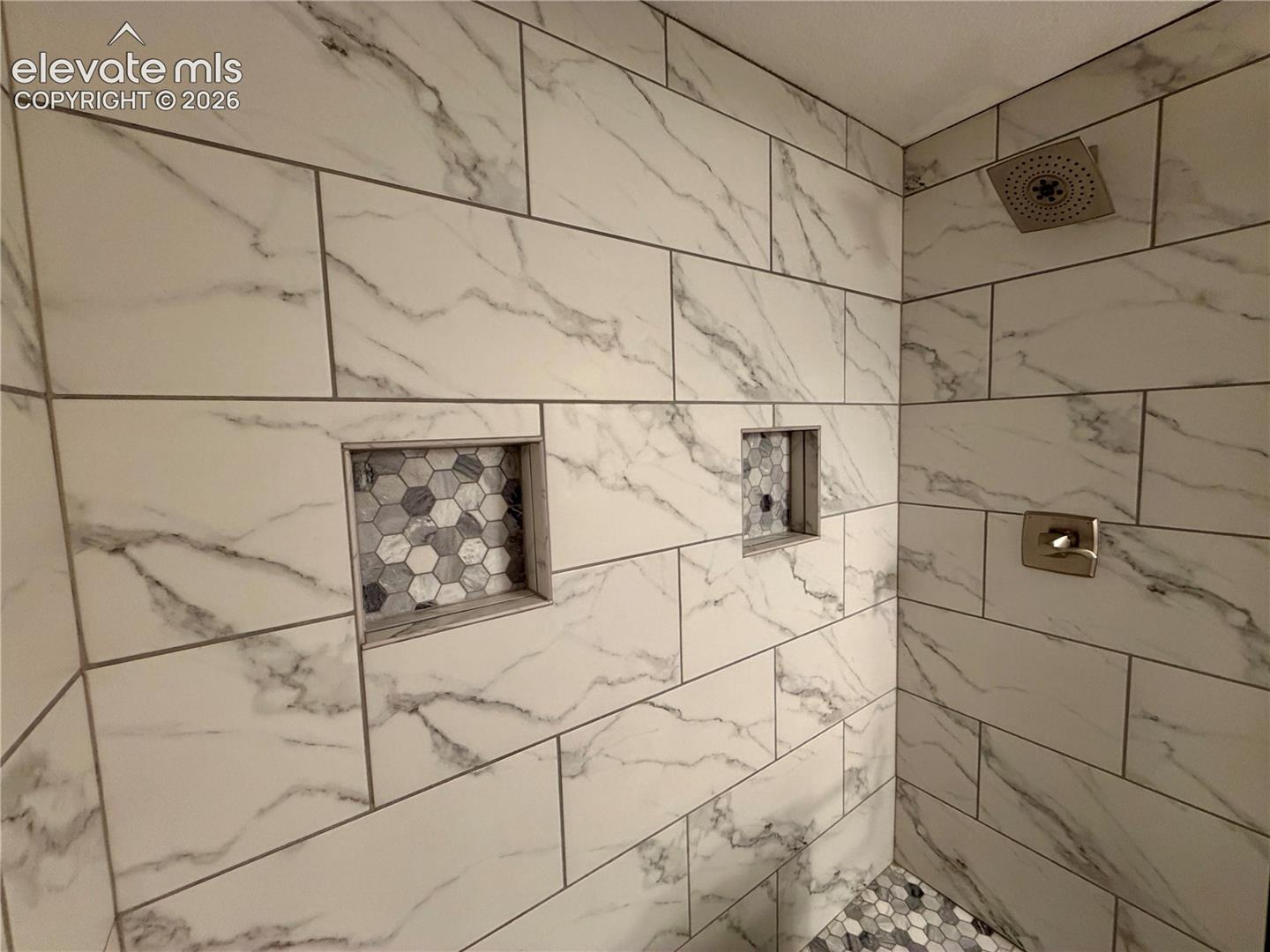 Basement Bathroom-Shower featuring large format marble-look wall tiles, two recessed niches with hexagonal mosaic tile backing, and a brushed nickel shower fixture with a rain shower head