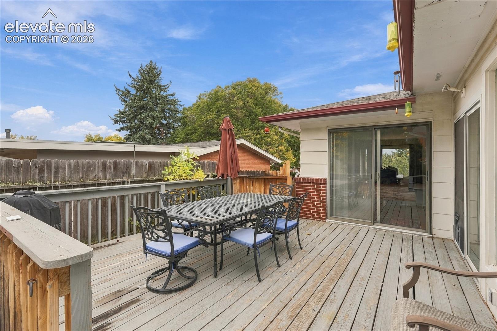 Elevated wood-plank deck featuring a wooden railing, red brick accent siding, and sliding glass door access