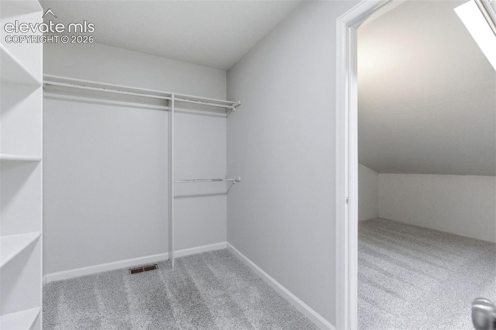 Walk-in closet with built-in shelving, two hanging rods, and light-grey carpeting