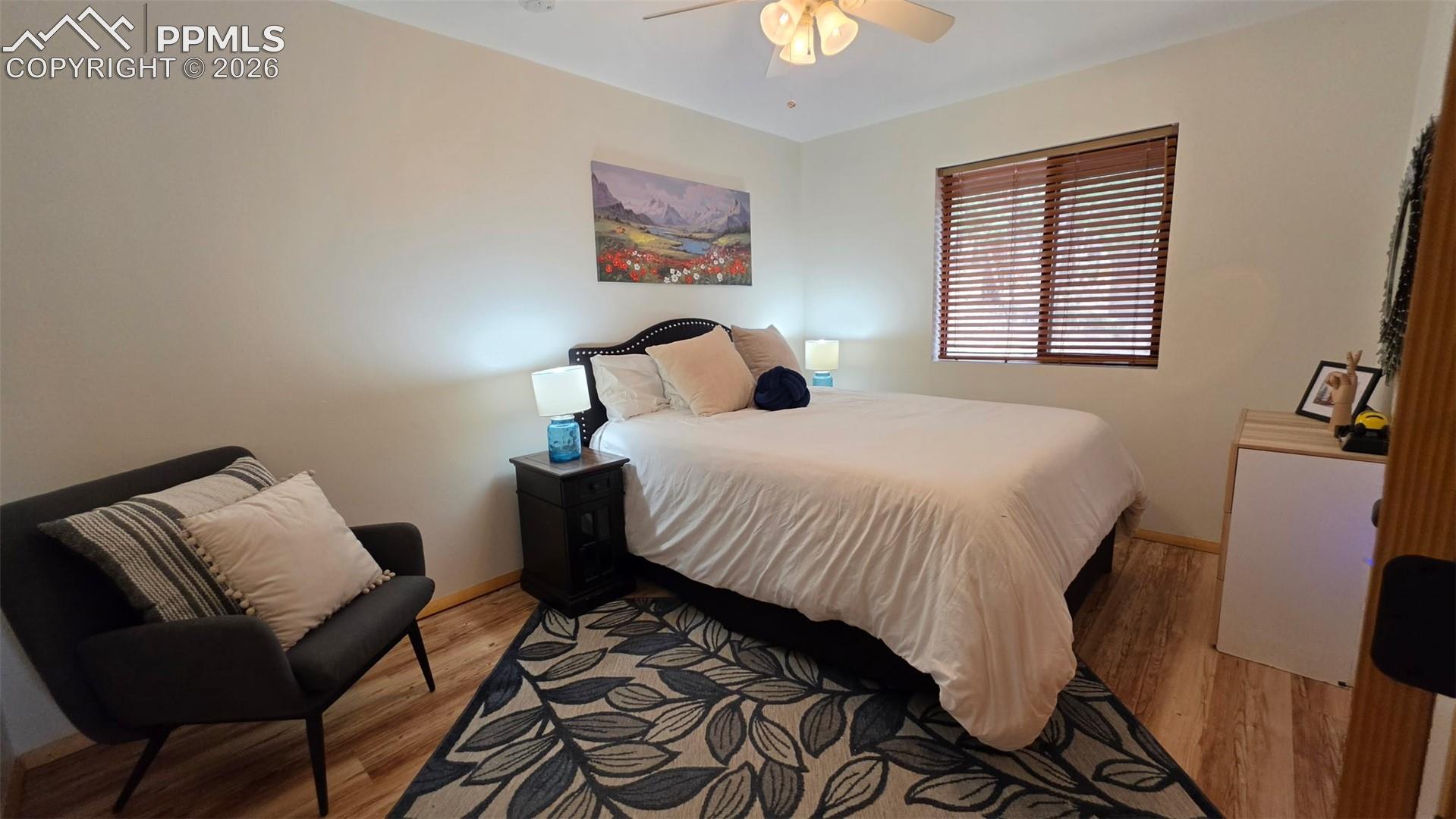 Bedroom featuring wood-finish flooring, a ceiling fan with light fixture, and a window with wood blinds