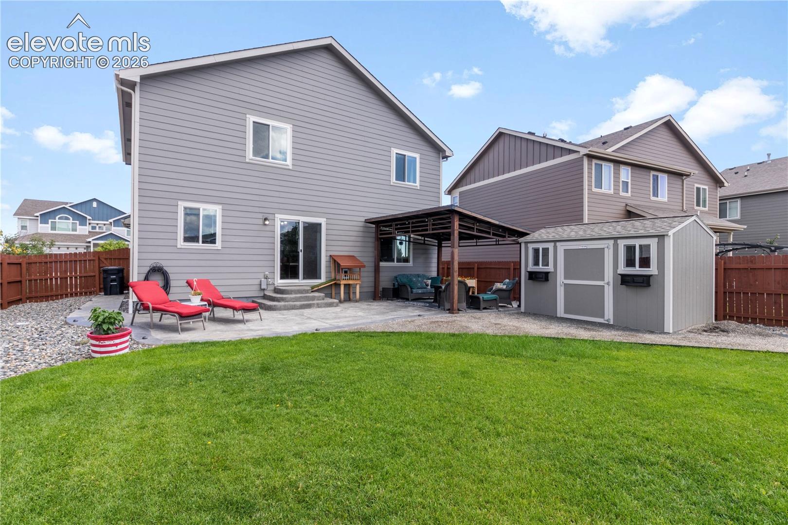 Expansive fenced backyard featuring a manicured lawn, concrete patio, covered outdoor structure, and a storage shed