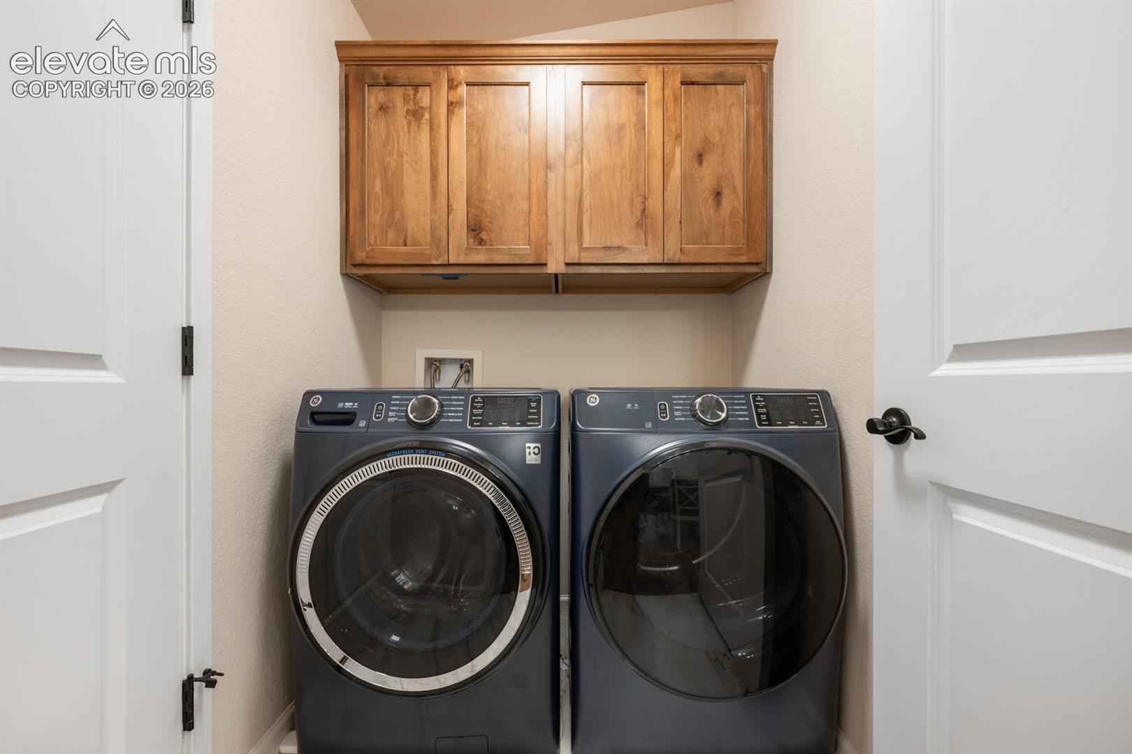 Laundry area featuring wood-finish cabinetry, white paneled doors, and matte black hardware