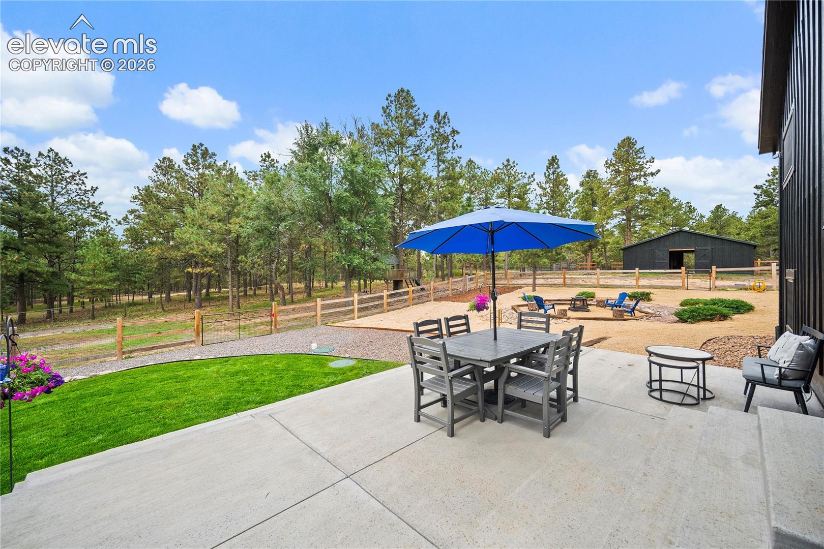 Rear concrete patio featuring a manicured lawn, gravel hardscaping, a stone fire pit, and a detached outbuilding