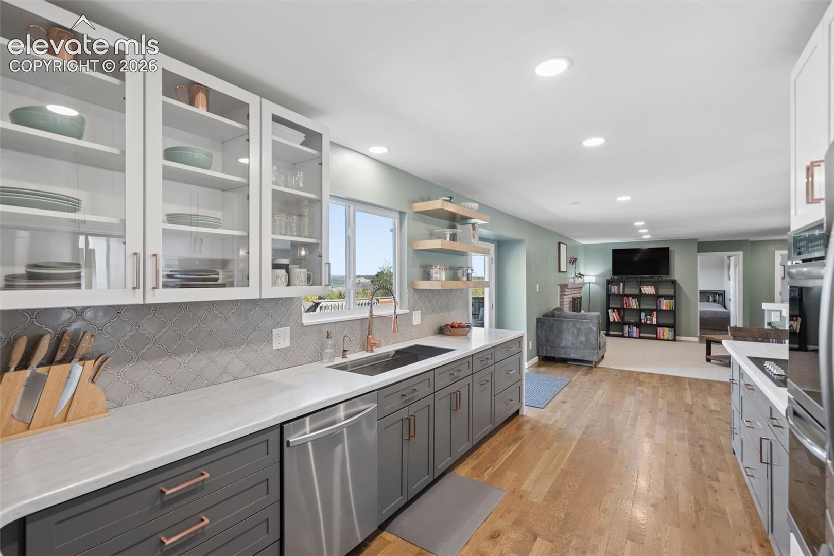 Kitchen featuring charcoal-toned lower cabinetry, white upper cabinets with glass-panel doors, wood-finish flooring, patterned tile backsplash, and built-in wall oven