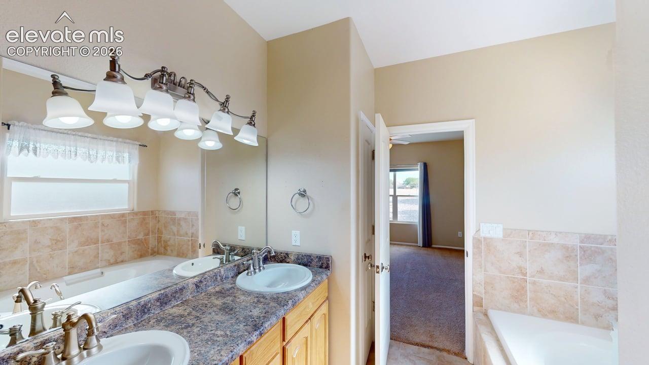Dual vanity with integrated sinks, full-width mirrors, warm wood-finish cabinetry, and a built-in tub with a tile surround