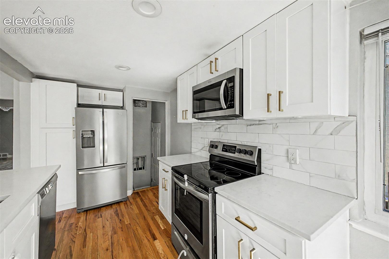 Kitchen featuring white shaker cabinetry, stainless steel appliances, light-toned wood-finish flooring, and white countertops