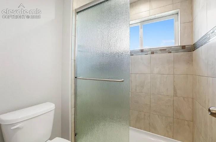 Shower enclosure featuring textured glass sliding doors, neutral-toned wall tile, decorative mosaic tile accents, and a window