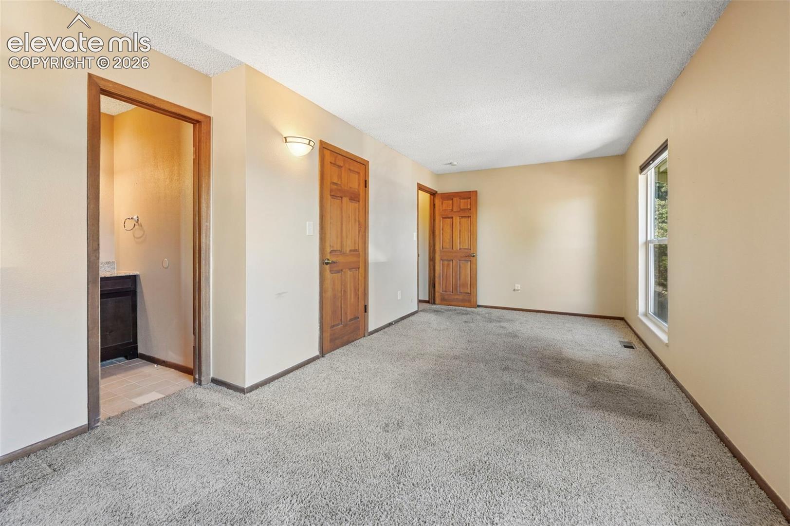 Room featuring neutral wall tones, six-panel wood-finish interior doors, carpeted flooring, and a wall-mounted sconce