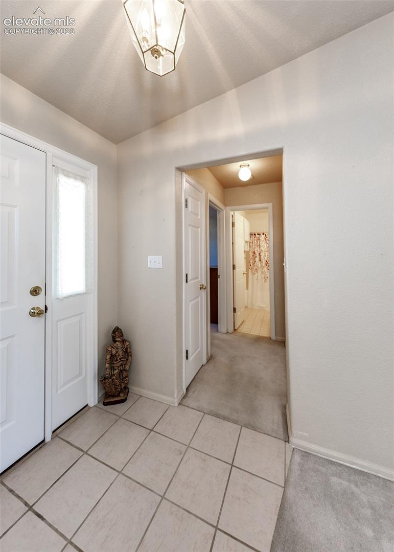 Entryway featuring neutral-toned tile flooring, a paneled door with a vertical glass insert, and a geometric pendant light fixture