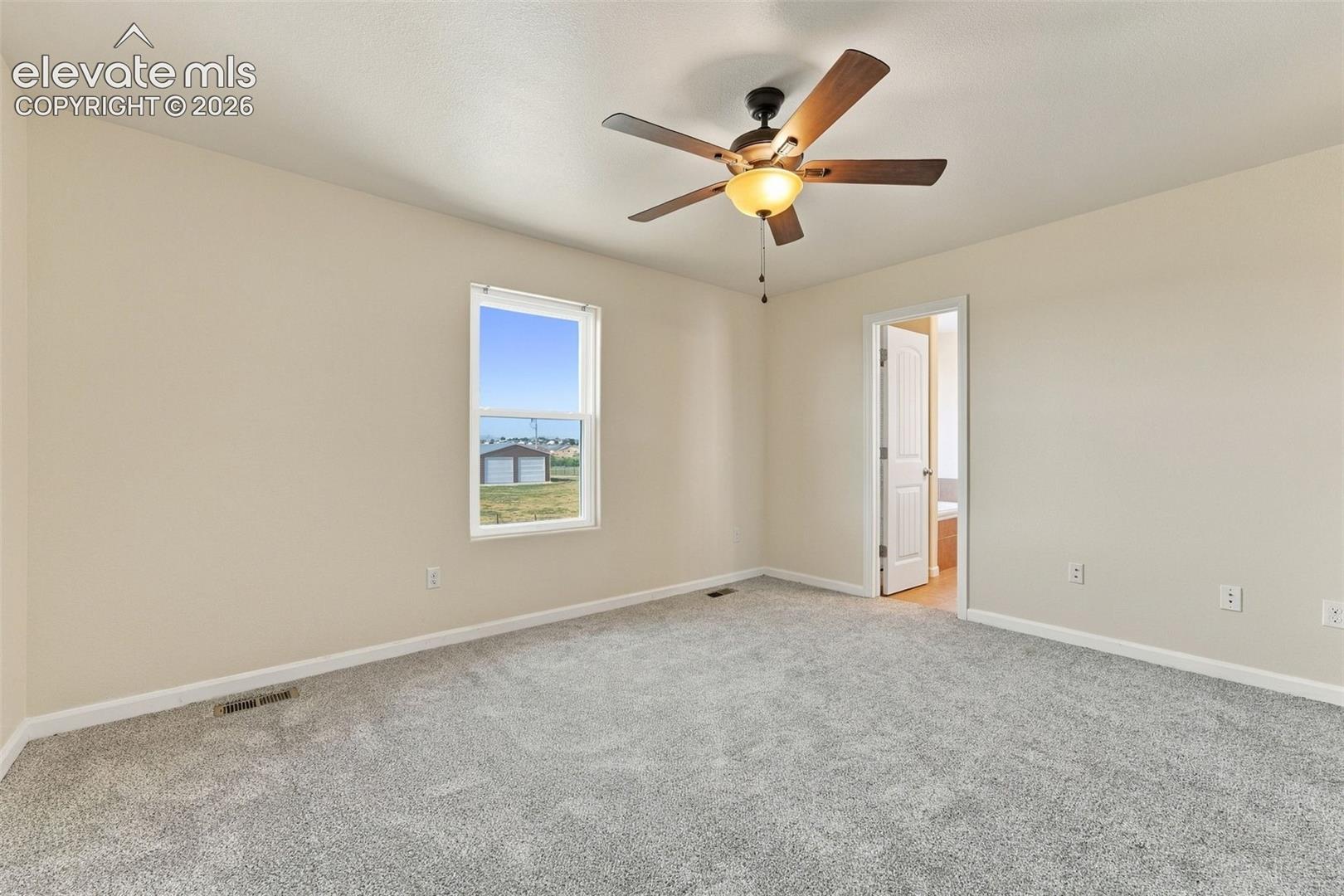 Neutral-toned interior room featuring wall-to-wall carpeting, a single-pane window, and a multi-blade ceiling fan with integrated lighting