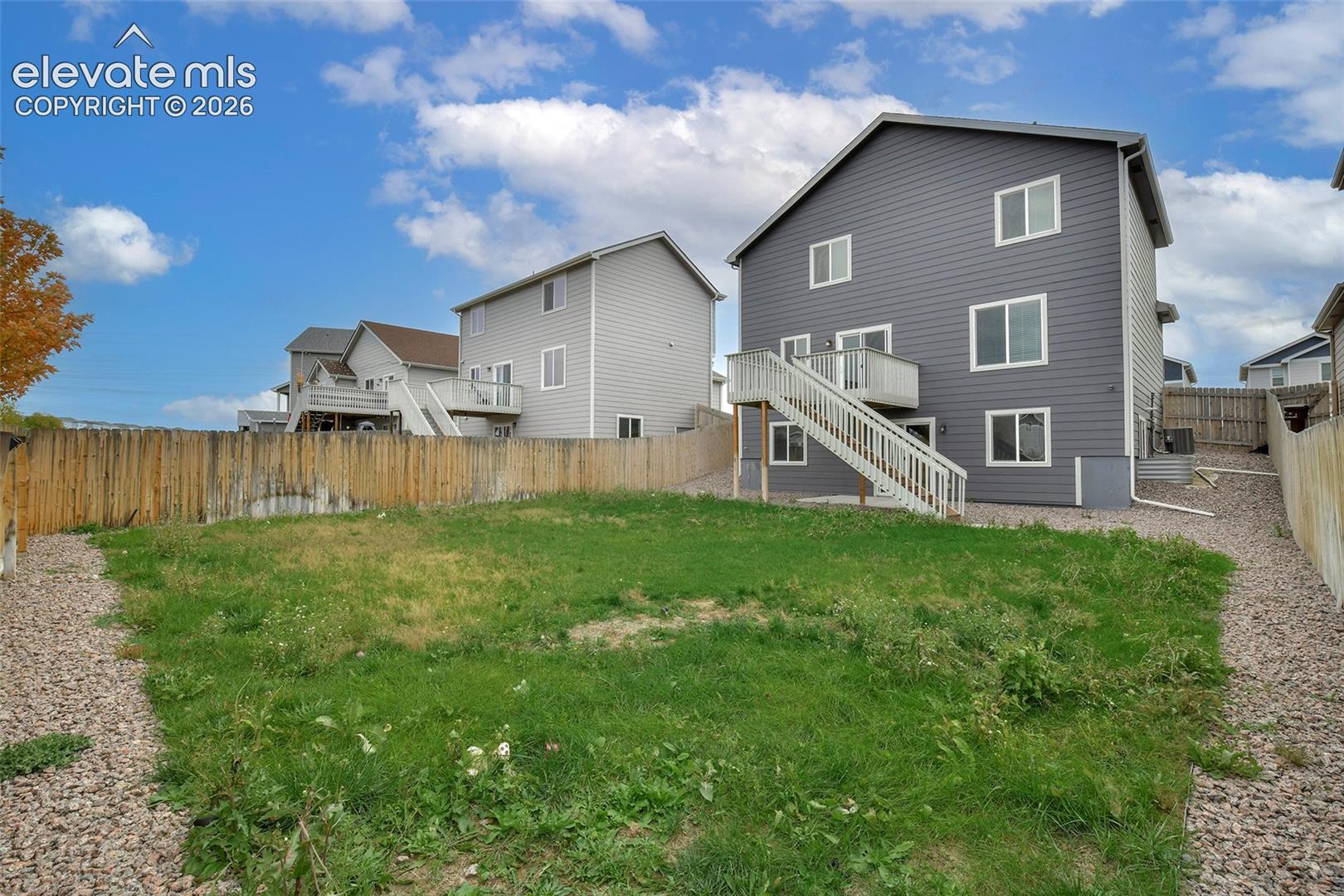 Rear exterior featuring horizontal lap siding, a raised wooden deck with staircase, and a fenced backyard with gravel perimeter bordering