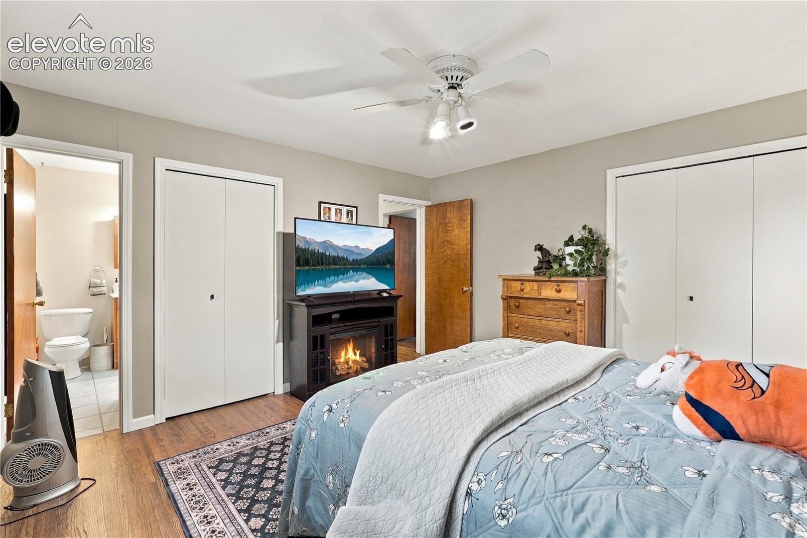 Room featuring wood-finish flooring, dual closets with white bi-fold doors, and a ceiling fan with integrated lighting