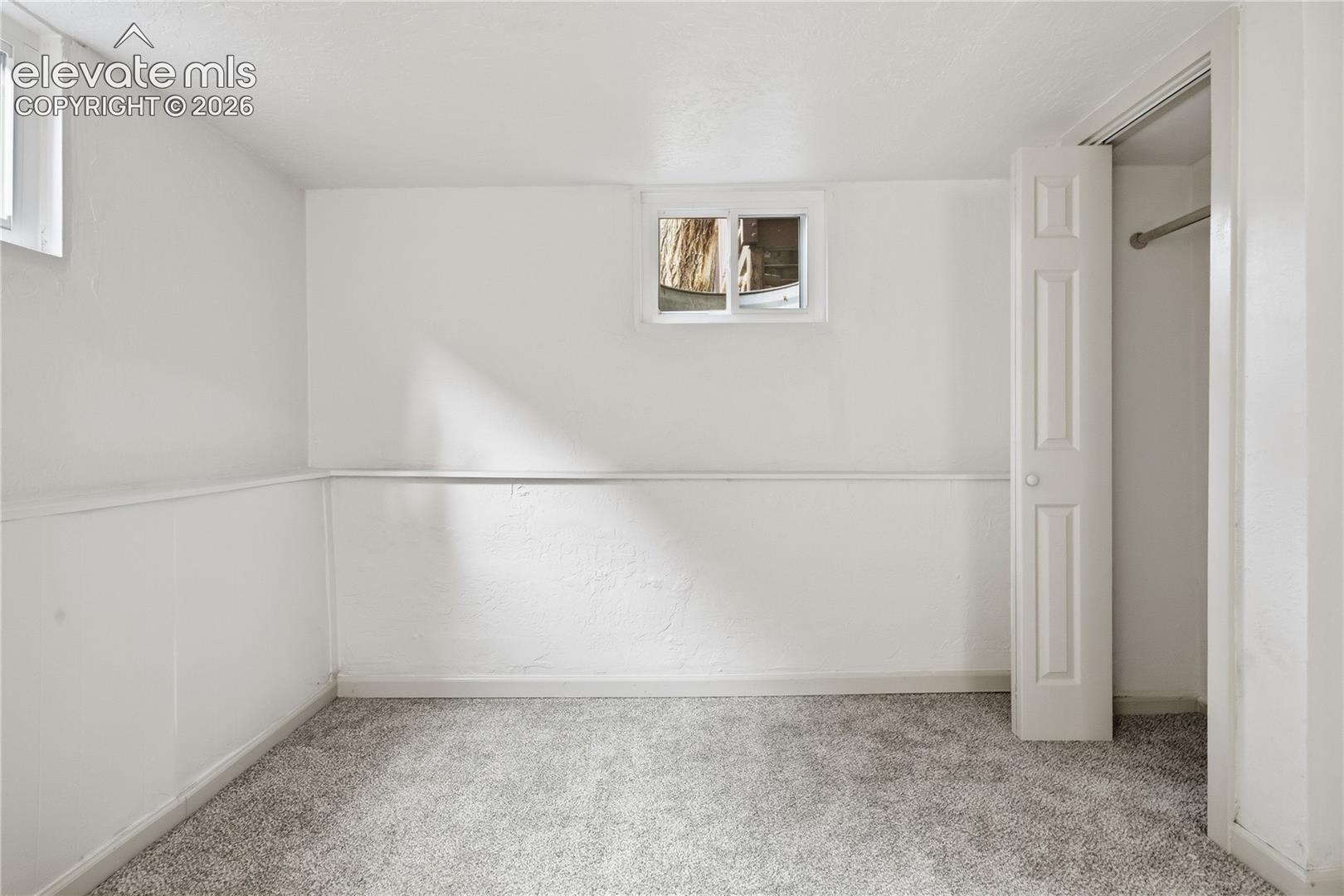 Neutral-toned carpeting, white wainscoting, sliding windows, and a built-in closet with a hanging rod
