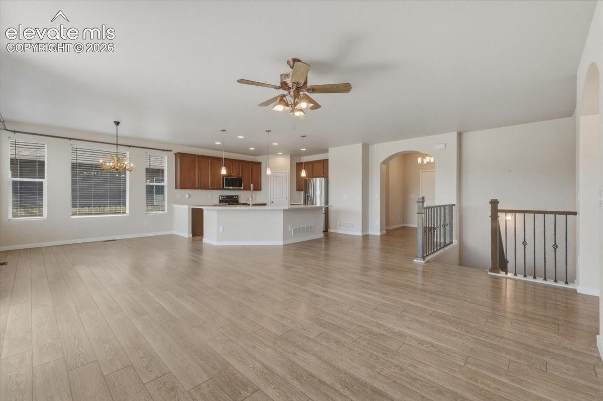 Open-concept living area featuring wood-finish flooring throughout, a ceiling fan with integrated lighting, and multiple windows with blinds